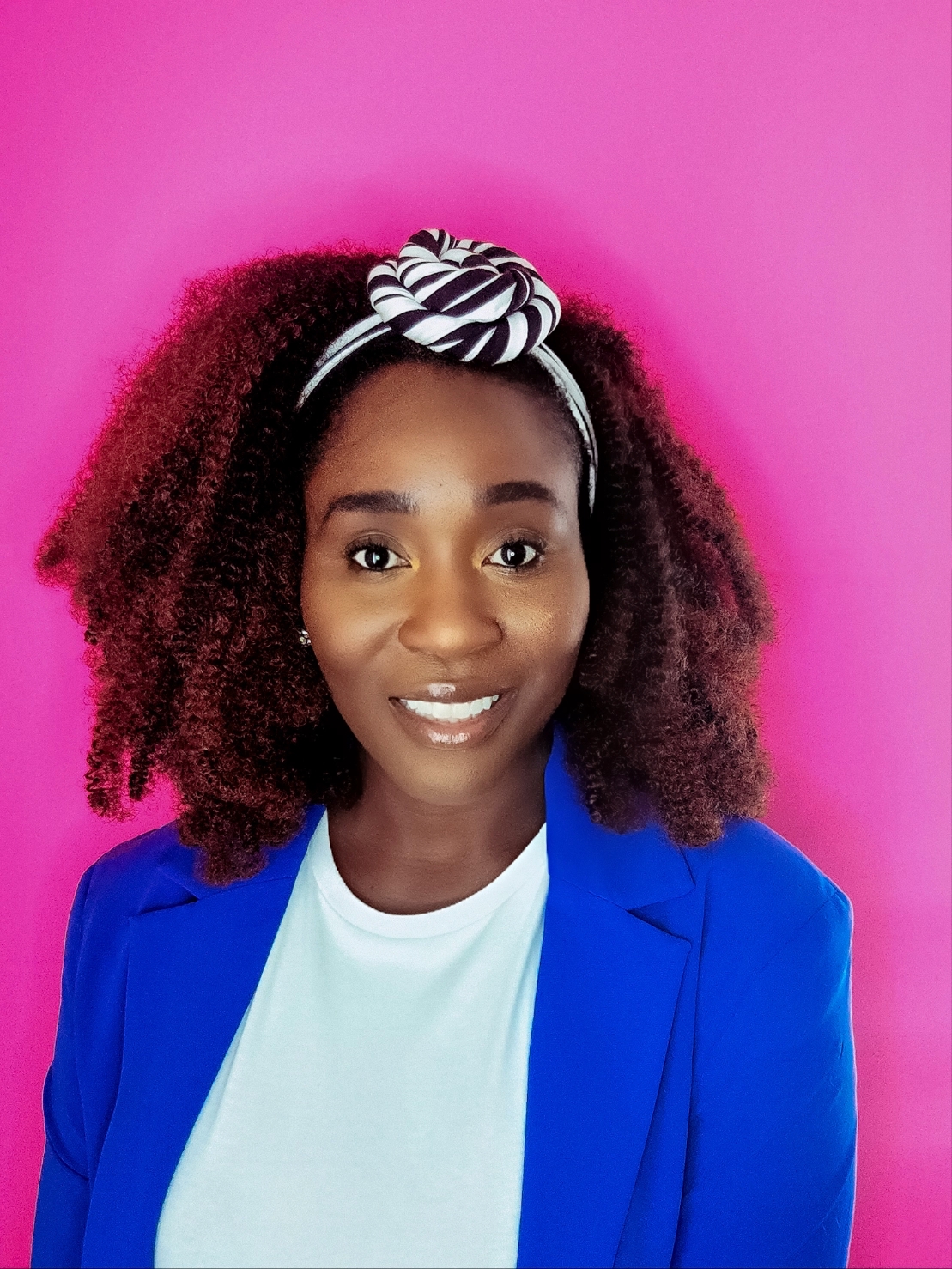 Image of Donnica smiling in a blue blazer against a hot pink background
